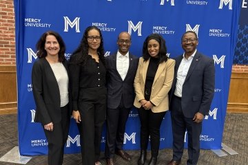  Lauder Institute Alumni and Mercy University School of Business Dean Victor Petenkemani pose in front of step and repeat after fireside chat panel celebrating Black History Month