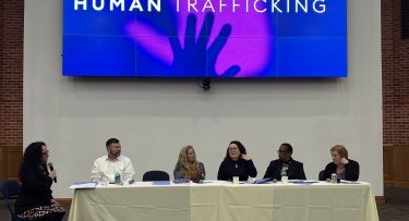 Moderator and guest panelists seated behind table at the front of the room for a human trafficking panel discussion at Mercy University