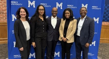  Lauder Institute Alumni and Mercy University School of Business Dean Victor Petenkemani pose in front of step and repeat after fireside chat panel celebrating Black History Month